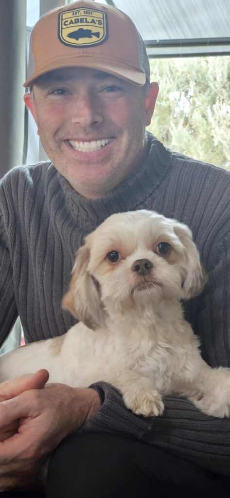 Man smiling with a small white dog.